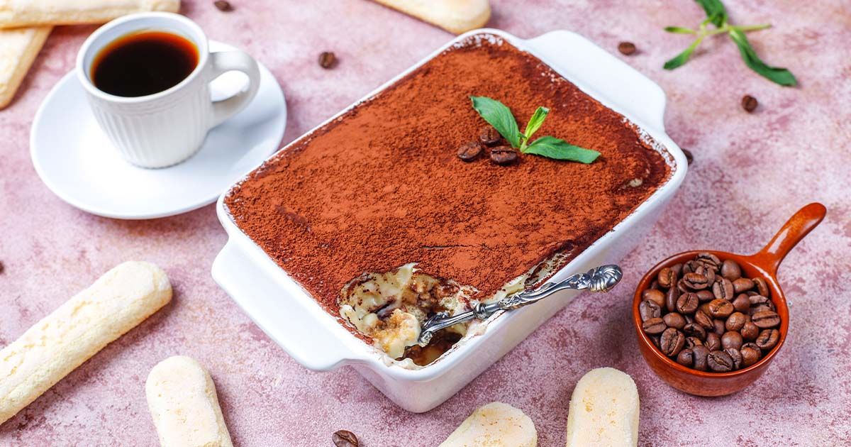 Tiramisu surrounded by lady fingers, coffee beans, and coffee.